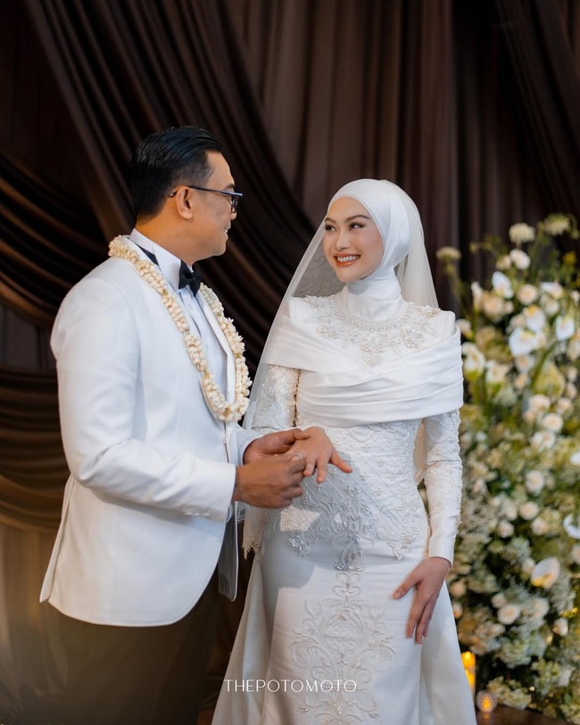 Gaya hijab Indah Nada Puspita menampilkan siluet yang rapi dan clean look yang menutup leher dengan sempurna. Dipadukan dengan veil brokat panjang yang menjuntai indah, hijab ini sukses memberikan kesan pernikahan modern yang mewah dan berkelas. Foto: Dok. Instagram @thepotomoto.