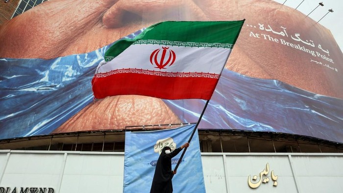 Seorang wanita melambaikan bendera Irandi depan billboard anti-AS di Alun-alun Valiasr, Teheran (dok. AFP)