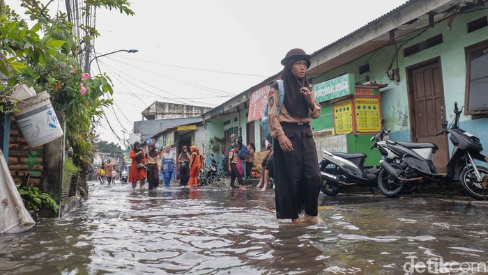 Sejumlah anak sekolah terlihat pulang dengan melintasi genangan banjir di Jalan Dermaga Baru, Klender, Jakarta Timur, Rabu (20/5/2026). Genangan air muncul usai hujan deras mengguyur kawasan Jakarta sejak pagi hari.
