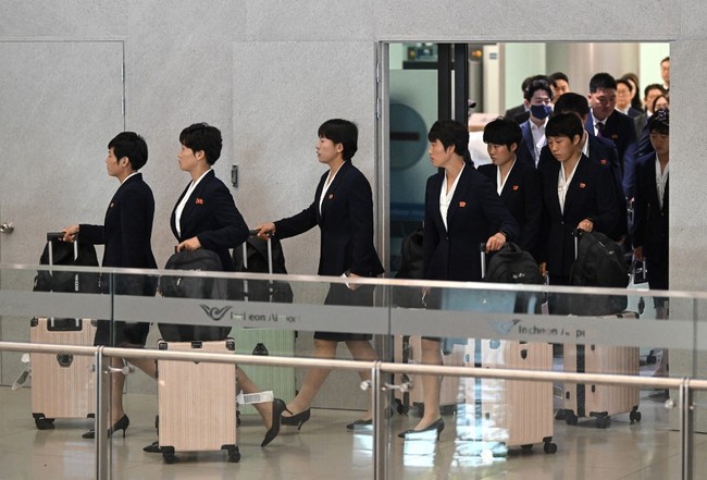 Sejak keluar dari area kedatangan bandara, para pemain langsung mencuri perhatian. Mereka terlihat mengenakan blazer gelap dan rok sepanjang lutut dengan model serupa, lengkap dengan koper warna pink yang sama.  Foto: AFP/JUNG YEON-JE