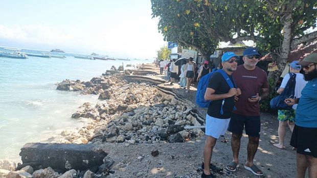 Sejumlah wisatawan berjalan di sisa jalan yang amblas dikikis abrasi di pantai Banjar Nyuh, Nusa Penida, Klungkung, Bali, Rabu (20/5/2026) pagi. (Dok.Istimewa)