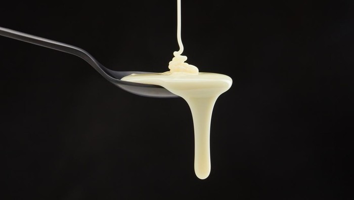 White cream or condensed milk dripping in a spoon and from a spoon on a black background. Shallow depth of field