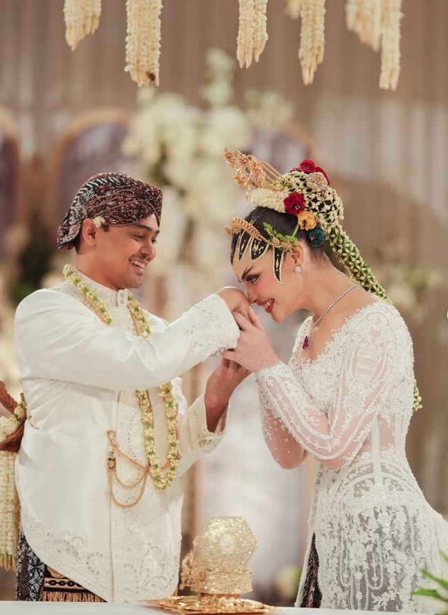 Agassi Revano tampil gagah mengenakan beskap putih beraksen bordir dan payet berkilau. Ia memadukannya dengan kain batik bernuansa cokelat gelap khas Yogyakarta. Detail kalung melati, keris, serta aksesori rantai emas pada beskap menambah kesan tradisional. Foto: Instagram/@tengkunadiraadn