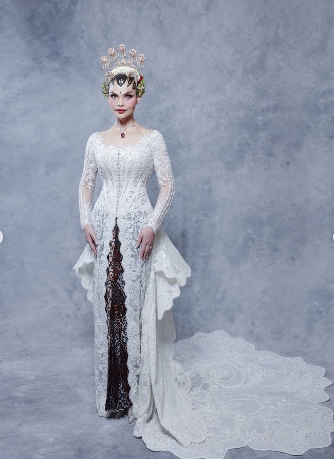 Tengku Nadira mengenakan kebaya putih rancangan desainer Eddy Betty. Kebaya tersebut dilengkapi detail bordir dan payet yang rumit. Siluet kebaya dibuat fit body sehingga menampilkan kesan anggun dan feminin. Bagian rok dan ekor kebaya memiliki detail layer yang artistik, membuat penampilannya terlihat dramatis namun tetap elegan. Foto: Instagram/@tengkunadiraadn