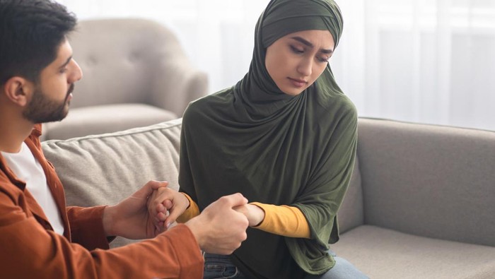 Marital Crisis. Unhappy Middle Eastern Couple Holding Hands Sitting Together On Sofa Indoors. Bad Relationship, Forced Marriage Problem And Family Conflicts Concept. Selective Focus