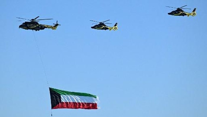 A Kuwaiti police Eurocopter EC225 Super Puma helicopter flies with a giant Kuwaiti national flag below, followed by two Eurocopter EC155 police helicopters during an airshow commemorating Kuwaits 64th Independence Day in Kuwait City on February 25, 