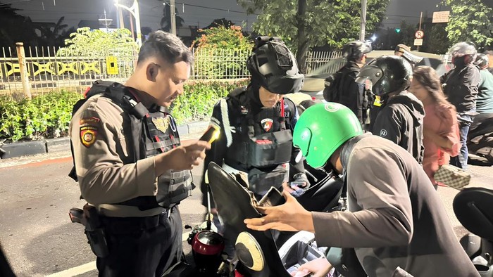 Anggota Brimob Polda Metro Jaya membantu mengevakuasi driver ojol yang terkapar di pinggir jalan di Jaktim, Jumat (29/5/2026) dini hari.