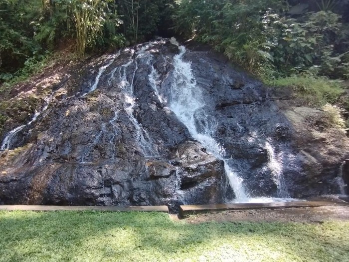 Air mengalir melalui celah bebatuan bak air terjun di Taman Magenda, Gianyar, Bali. Air terjun itu diapit oleh kolam alami dan Pura Taman Magenda.