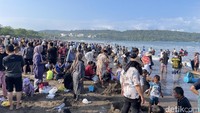 Wisatawan berdesakan berenang, bermain pasir, dan berebutan tempat duduk untuk menikmati suasana pantai. Sebagian wisatawan melakukan kegiatan makan bersama di bawah pohon.