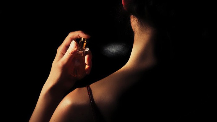 Woman sprays perfume on her neck with a black background.