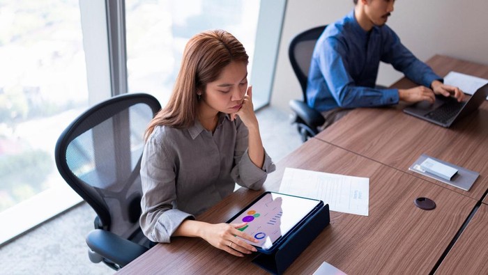 Two colleagues work quietly at a modern office table, reviewing charts and documents on a tablet.