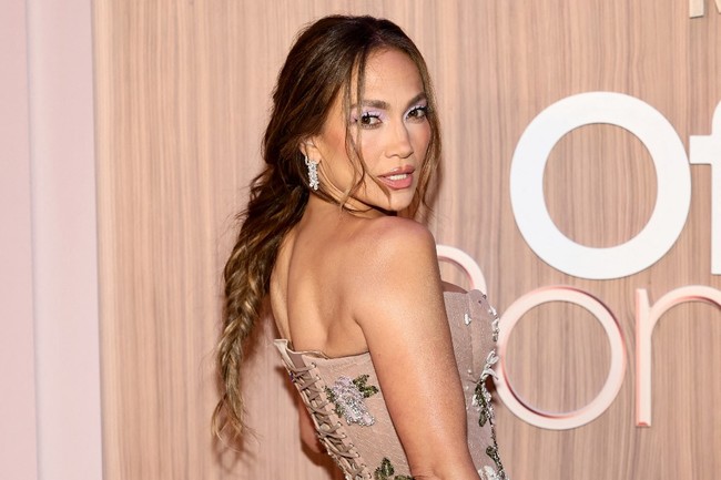 J.Lo melengkapi busananya dengan clutch warna bronze metalik dan sepasang anting berlian dari koleksi Harry Winston. Untuk menambah kesan seksi dan glamor, mantan istri aktor Ben Affleck ini memilih riasan wajah bernuansa nude dengan sentuhan shimmer dan lipstik warna natural yang dibubuhi lip gloss, menonjolkan bibir plumpy. Foto: Getty Images via AFP/THEO WARGO