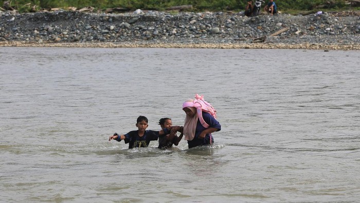 Orang tua siswa gendong anaknya di bahu saat melintasi sungai Meureubo untuk berangkat ke Sekolah Dasar Negeri (SDN) Alue Lhok dari Desa Canggai menuju ke Desa Jambak, Kecamatan Pante Ceureumen, Aceh Barat, Aceh, Jumat (5/6/2026). Sejak empat hari terakhir para siswa SDN Alue Lhok terpaksa mengarungi aliran sungai menuju kesekolah untuk mengikuti ujian kenaikan kelas guna mempersingkat jarak tempuh delapan kilometer karena jembatan gantung penghubung antar desa rusak pascabencana banjir bandang akhir November 2025 lalu tak kunjung diperbaiki. ANTARA FOTO/Syifa Yulinnas/YU