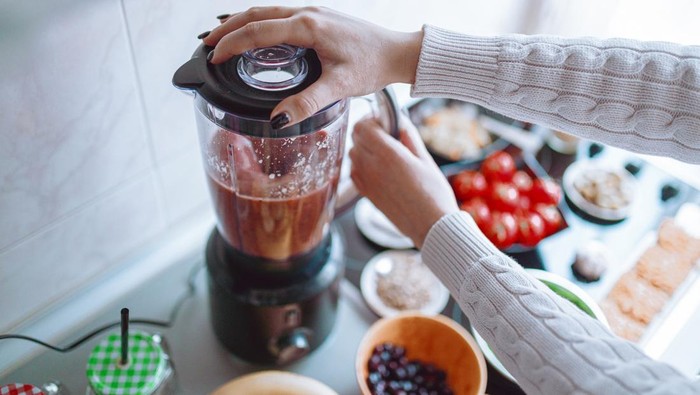 Woman making tasty and healthy fruit and vegetable smoothie in the kitchen at home
