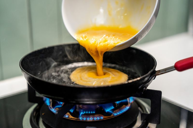 A hand gently folds a fluffy omelet in a pan, beside a perfectly sizzling fried egg. Close-up A hand expertly cooks a golden omelet and a sunny-side-up egg in a hot pan.