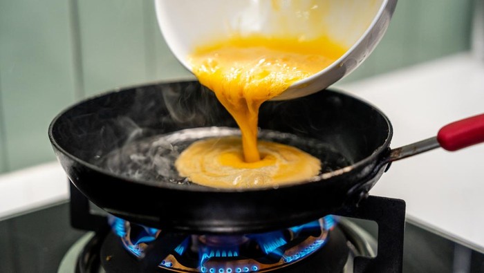 A hand gently folds a fluffy omelet in a pan, beside a perfectly sizzling fried egg. Close-up A hand expertly cooks a golden omelet and a sunny-side-up egg in a hot pan.