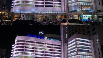 Perbandingan hasil pemotretan malam menggunakan Galaxy A57 5G (atas) dan Galaxy A37 5G (bawah). Keduanya mampu mengontrol sumber cahaya terang seperti lampu gedung dan papan nama tanpa kehilangan detail bangunan. Perbedaan utama terlihat pada karakter pemrosesan warna dan tingkat kecerahan gambar. Foto: Rizky Nur Amalia/detikINET