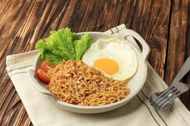Indomie Goreng or Mie Goreng, Indonesian Popular Instant Noodle. Served with Sunny Side Egg, Tomato, Cucumber. Warmindo, Warkop, Ropang.Warmindo Mie Goreng dan Roti Bakar