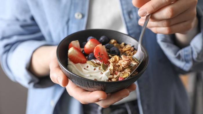 Woman eating tasty granola with berries, yogurt and seeds, closeup