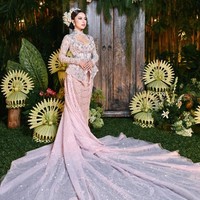 Bagian bawahnya mengalir dramatis dengan ekor panjang transparan bertabur detail berkilau, menciptakan efek megah saat ia berdiri di tengah dekorasi bernuansa tropis khas Bali. (Foto: Instagram/@jennifercoppenreal20)