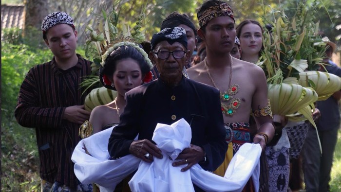 Pemuka adat menuntun sepasang muda mudi pembawa biji kopi lanang (laki-laki) dan wadon (perempuan) yang sudah dikawinkan saat tradisi upacara temanten kopi di perkebunan Kopi De Karanganjar, Blitar, Jawa Timur, Minggu (14/6/2026). Tradisi Temanten Kopi merupakan ritual memilih dan memetik kopi lanang dan wadon terbaik yang kemudian digiling bersamaan sebagai penanda masuknya musim panen dan giling biji kopi yang rutin dilakukan masyarakat perkebunan kopi lereng Gunung Kelud sebagai wujud rasa syukur atas hasil panen yang melimpah serta kualitas biji kopi yang baik. ANTARA FOTO/Irfan Anshori/kye