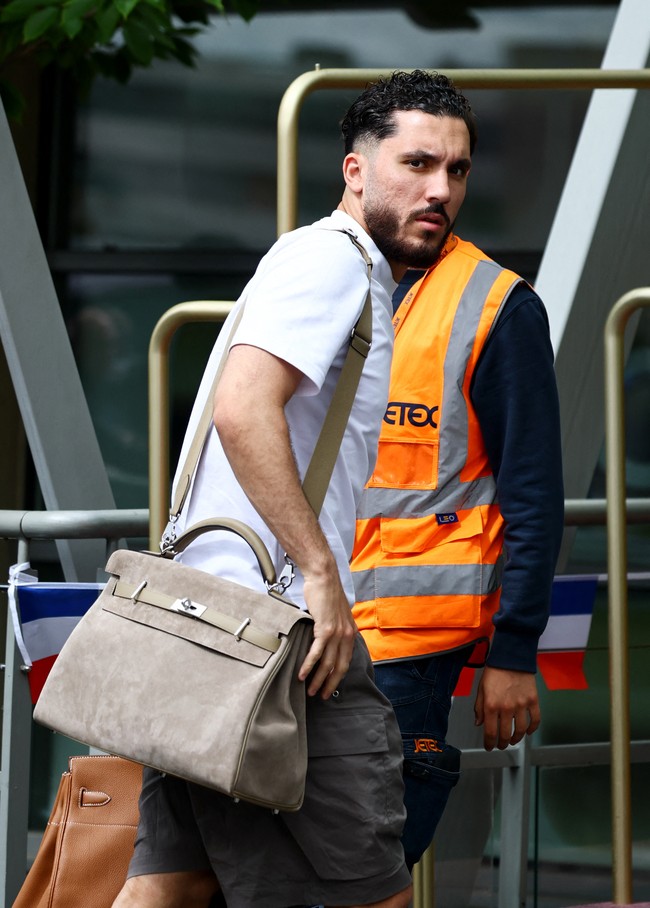 Bertolak ke Amerika Serikat dari bandara Paris-Le Bourget pada Rabu (10/6/2026), Rayen Cherki kedapatan memakai tas Hermès Haut à Courroies coklat pucat berbahan suede. Outfit kasualnya yang terdiri dari polo-shirt putih, celana pendek cargo coklat gelap, dan sneakers putih mendadak terasa elevated berkat tas tersebut. (Foto: REUTERS/Sarah Meyssonnier)