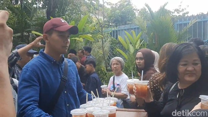 Momen staf Presiden ke-7 RI, Joko Widodo (Jokowi), membagikan es teh kepada warga yang tengah mengantre untuk berfoto di Sumber, Banjarsari, Solo, Senin (15/6/2026).