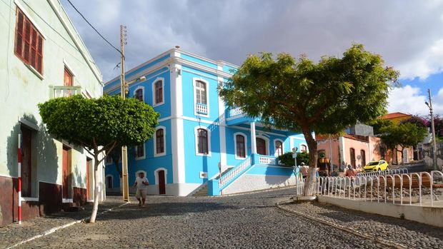 Dari Kejutan Piala Dunia ke Surga Atlantik, Pesona Tanjung Verde Mencuri Perhatian A man walking down a street and other men standing by a tree in Sao Felipe, small capital of the island of Fogo in Cabo Verde off the coast of Senegal. Sao felipe is a small town with colourful houses and yellow taxis. It was a sunny day in December . There were a yellow car parked in front of colorful houses