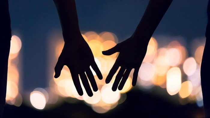 Man and womans hands coming together facing the city night lights.