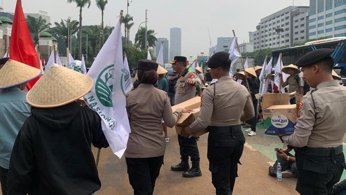 Polisi membagikan air mineral dan snack ke massa petani bercaping yang aksi di DPR, Senin (22/6/2026).