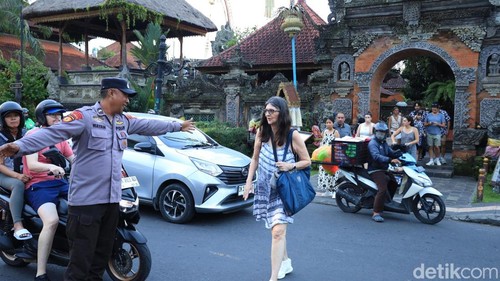 Personel Polsubsektor Catus Pata Polsek Ubud Aipda Wayan Arip Dipa saat menyeberangkan para turis asing di catus pata Ubud, Senin (22/6/2026).