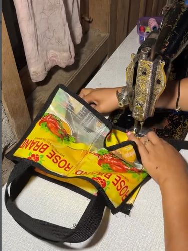Daur ulang kreatif limbah plastik kemasan minyak goreng menjadi tas jinjing belanja yang unik, estetis dan bernilai guna menggunakan sebuah mesin jahit.