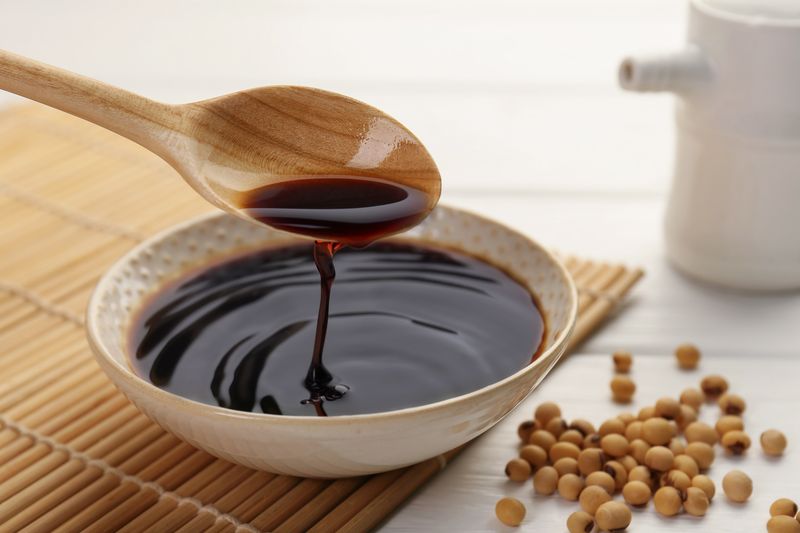ilustrasi kecap manis Taking tasty soy sauce from bowl with spoon on white wooden table, closeup