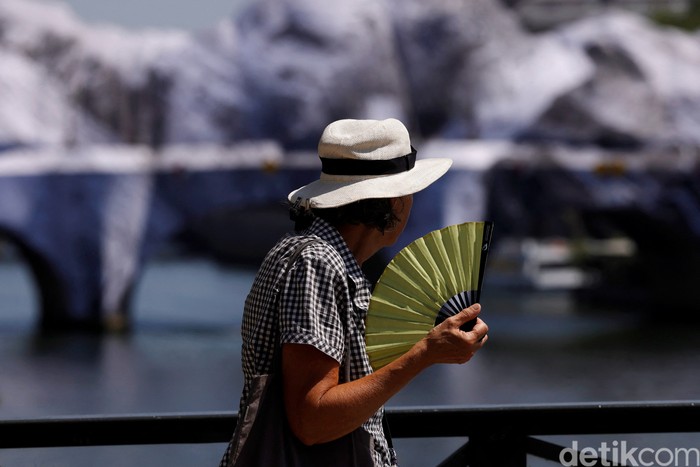 A person wearing a hat and holding a hand fan walks on the Pont des Arts bridge over the River Seine in Paris as temperatures rise during a heatwave affecting a large part of France, June 22, 2026. REUTERS/Alice Sacco