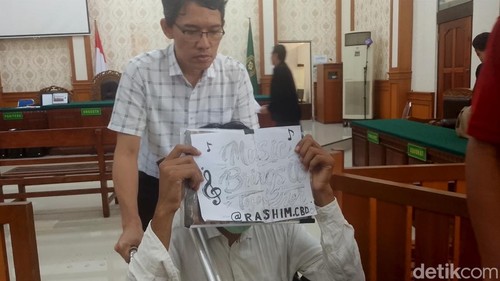 Terdakwa WN Belanda menunjukan kertas yang menutupi wajahnya bertuliskan Music Bring Us Together, seusai sidang di PN Denpasar, Selasa (23/6/2026).