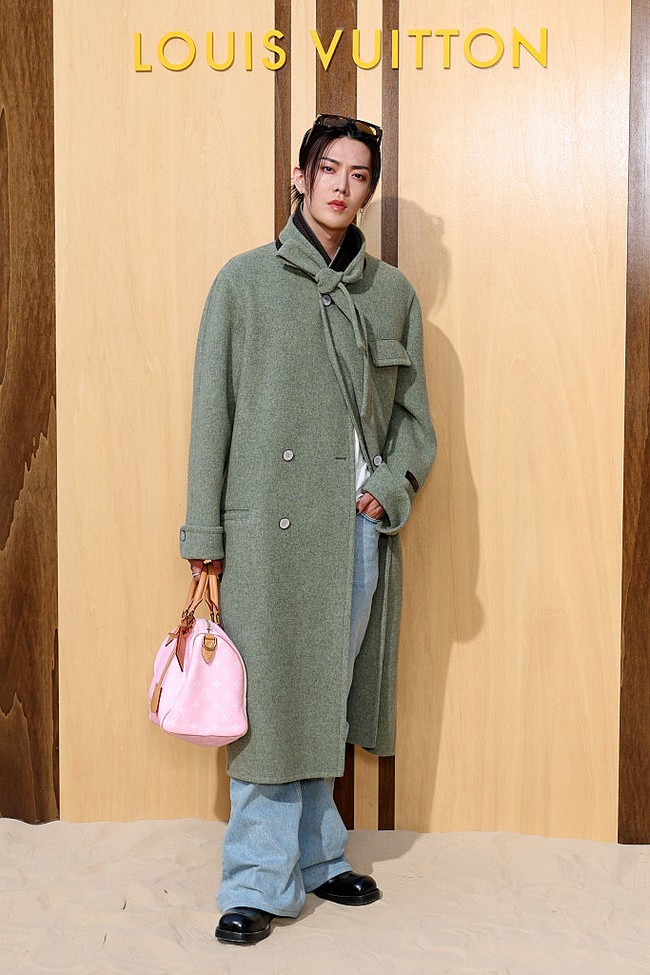 Tak ketinggalan, ada Yuta NCT yang tampil standout dengan hand bag berwarna pink. Saat berpose di photo call spot, ia berbalut trench coat hijau yang klasik dengan detail dasi leher yang unik, serta kacamata hitam Louis Vuitton yang disematkan di atas kepala. Foto: Getty Images