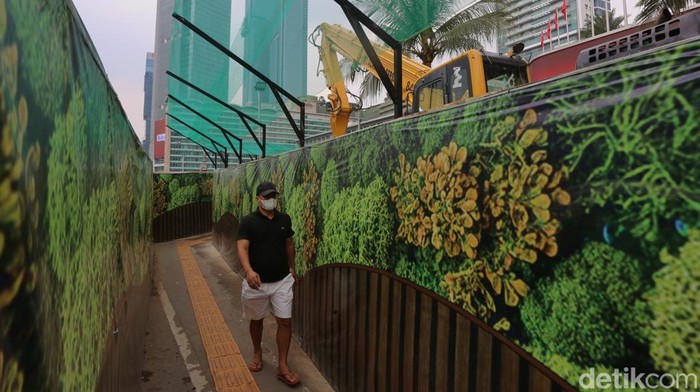 Pejalan kaki melewati jalur trotoar darurat yang didekorasi menyerupai lorong taman labirin di atas kawasan proyek pengembangan kawasan Stasiun MRT Bundaran Hotel Indonesia, Jakarta, Rabu (24/6/2026). Dekorasi ala taman labirin menjadi upaya menghindari suasana pengerjaan proyek infrastruktur yang kaku dan dingin. Begini penampakannya.