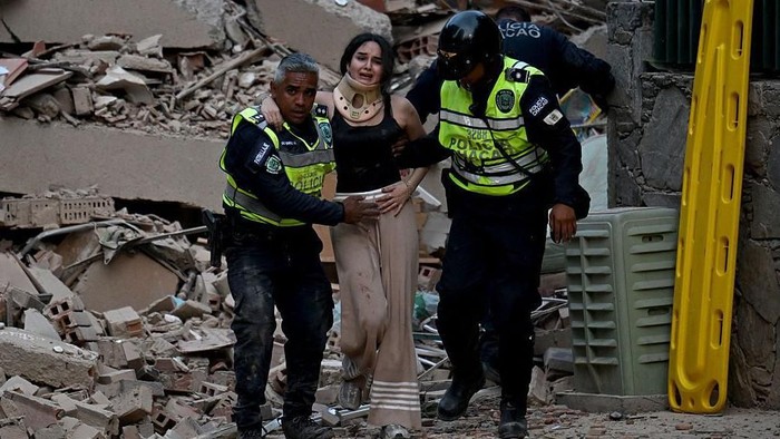 Polisi menolong seorang perempuan di antara reruntuhan bangunan di Caracas. (Getty Images)
