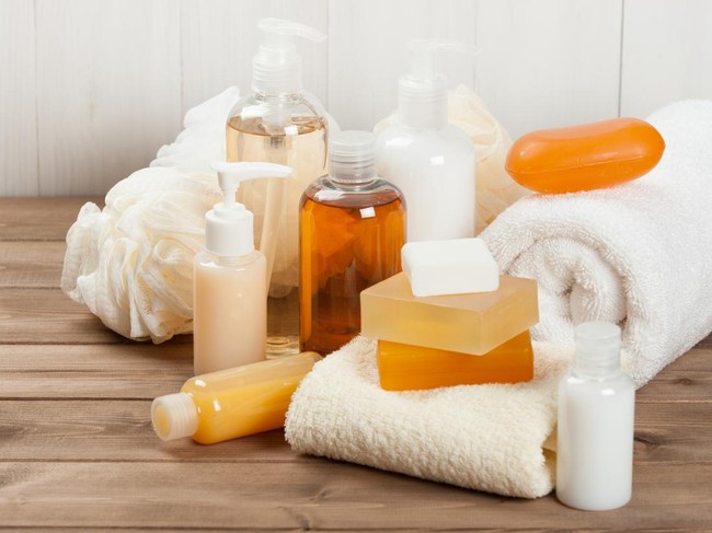 High angle view of woman hand choose cosmetics product for everyday skincare routine. Female hold glass bottle with dispenser over wooden shelf in bathroom. Self care, moisturizing, pampering concept