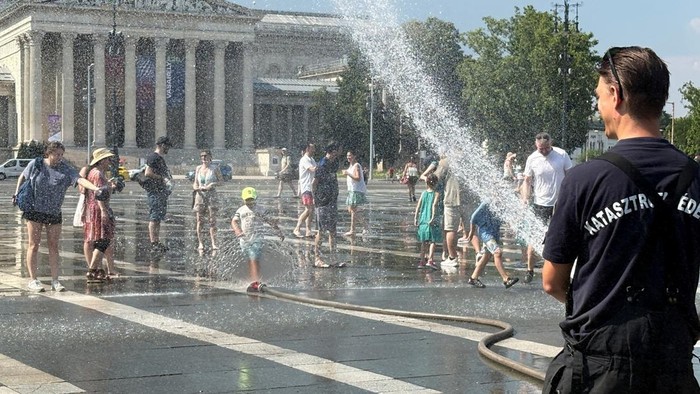 People enjoy as firefighters and police use water cannons to spray residents at Heroes Square to help them cool off during a severe heatwave in Budapest, Hungary, June 30, 2026. Picture taken with a mobile phone. REUTERS/Krisztina Fenyo