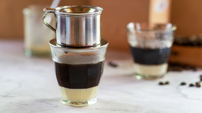 vietnamese coffee, dark roast coffee brewing with Vietnamese drip filter in glass on sweet condensed milk.