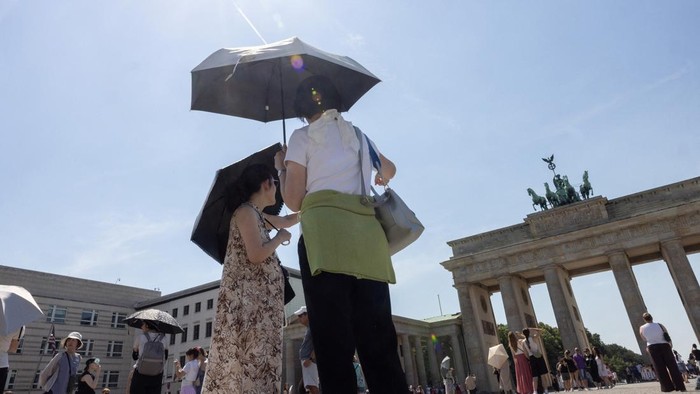 People shield themselves from the sun with umbrellas as they stand in front of the Brandenburg Gate during the ongoing heatwave in Berlin, Germany, June 27, 2026. REUTERS/Axel Schmidt