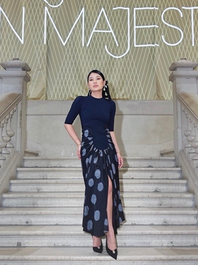 Pada 30 Juni, Putri Sirivannavari yang juga dikenal sebagai desainer sekaligus atlet berkuda itu menampilkan interpretasi yang lebih kontemporer lewat dua busana rancangan label Thailand, Pyvet. Saat mengunjungi Musée des Arts Décoratifs, ia mengenakan gaun midi dengan bodice rajut berwarna biru tua yang dipadukan rok dari kain Pha Mai Mudmee Lai Taem, sutra ikat tenun tangan asal Provinsi Roi Et karya penenun Thawisak Jattuwan. Potongan draperi modern berpadu harmonis dengan tekstil tradisional khas Thailand Timur Laut. (Foto: Instagram/@hrhsirivannavari)