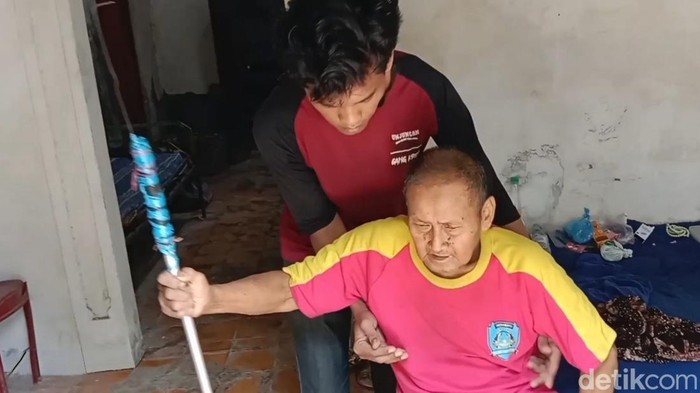 Irwan sedang membantu Casmita bangun dari tempat tidurnya.