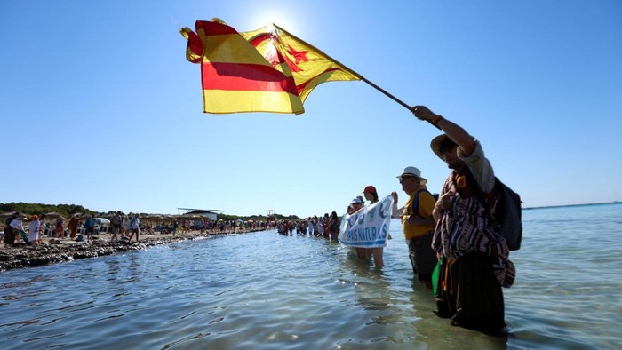 Ratusan aktivis dan warga menggelar aksi damai dengan membentuk rantai manusia di Pantai La Rapita, Mallorca, Spanyol, Minggu (5/7/2026), sebagai bentuk protes terhadap dampak pariwisata berlebihan (overtourism) di pulau tersebut. Aksi ini dilakukan untuk menyuarakan kekhawatiran atas meningkatnya tekanan terhadap kawasan pesisir alami yang dinilai semakin terancam akibat tingginya aktivitas wisata dan pembangunan. REUTERS/Francisco Ubilla