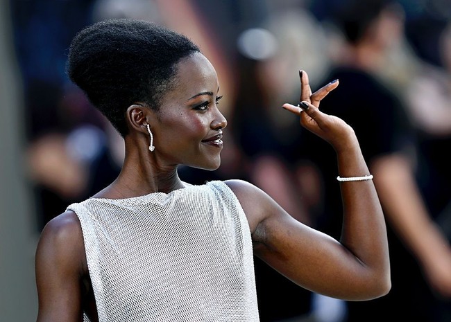 Lupita tampil dengan dewy makeup dan riasan mata bold, serta lipstik dark plum. Rambutnya ditata dengan sasak dan sanggul tinggi, mengaksentuasi tekstur rambut asli kering khas wanita Afrika. Foto: Gareth Cattermole/Getty Images/Gareth Cattermole