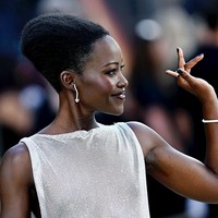 Lupita tampil dengan dewy makeup dan riasan mata bold, serta lipstik dark plum. Rambutnya ditata dengan sasak dan sanggul tinggi, mengaksentuasi tekstur rambut asli kering khas wanita Afrika. Foto: Gareth Cattermole/Getty Images/Gareth Cattermole