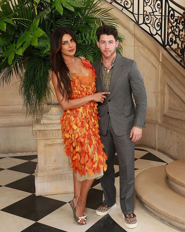 Priyanka tampil standout mengenakan gaun oranye cerah beraksen kelopak bunga dari koleksi Dior Cruise 2027. Sementara Nick tampil lebih kalem dengan setelan jas abu-abu dan dalaman kemeja kotak-kotak. Foto: Getty Images