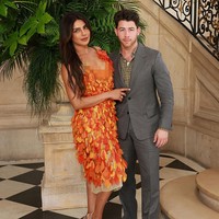 Priyanka tampil standout mengenakan gaun oranye cerah beraksen kelopak bunga dari koleksi Dior Cruise 2027. Sementara Nick tampil lebih kalem dengan setelan jas abu-abu dan dalaman kemeja kotak-kotak. Foto: Getty Images
