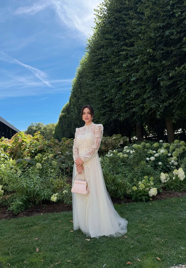 Dress yang dikenakan Shandy memiliki siluet yang jatuh lembut hingga mata kaki, menciptakan kesan anggun dan timeless. Bagian atas gaun dipenuhi detail bordir floral dan lace transparan pada dada, bahu, serta lengan panjang. Foto: Instagram/@shandyaulia